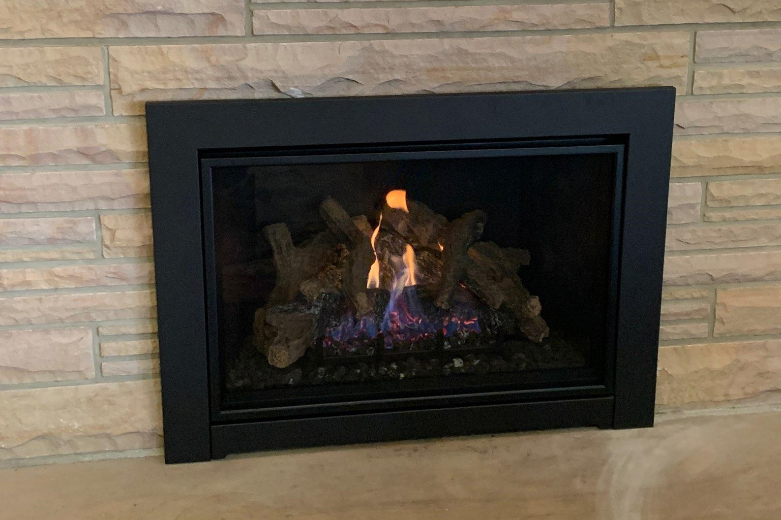 Empty stone fireplace with a metal log grate inside, showing soot marks on the firebox walls and hearth.