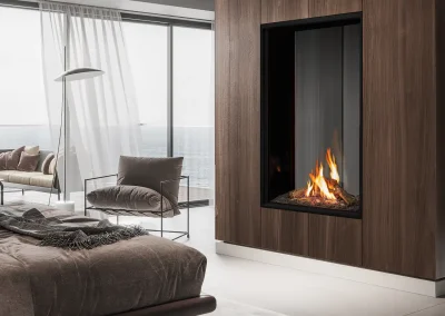 A modern bedroom featuring the Urbana Luxury Fireplace U33Tall see-through, with floor-to-ceiling windows, an ocean view, and cozy, elegant furnishings.