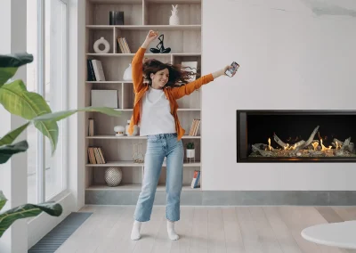 Energetic woman dancing in living room by music from smartphone in modern apartment home interior