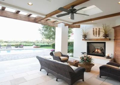 Stylish outdoor patio with a Valor gas fireplace, wicker seating, and a pergola ceiling, overlooking a pool and garden.