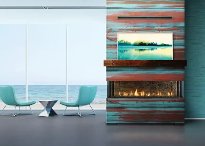 Modern coastal living space with turquoise chairs, ocean view windows, and a colorful wall-mounted fireplace beneath a landscape painting.