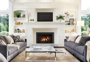 Bright modern living room with white built-in shelves, central fireplace and TV, gray sofas, and large windows with greenery views.