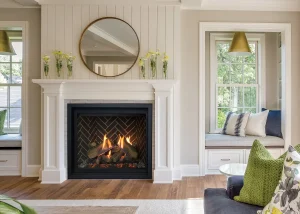 Bright living room with a white fireplace mantel, round mirror, and lit gas fireplace, accented by soft neutral decor and green throw pillows.