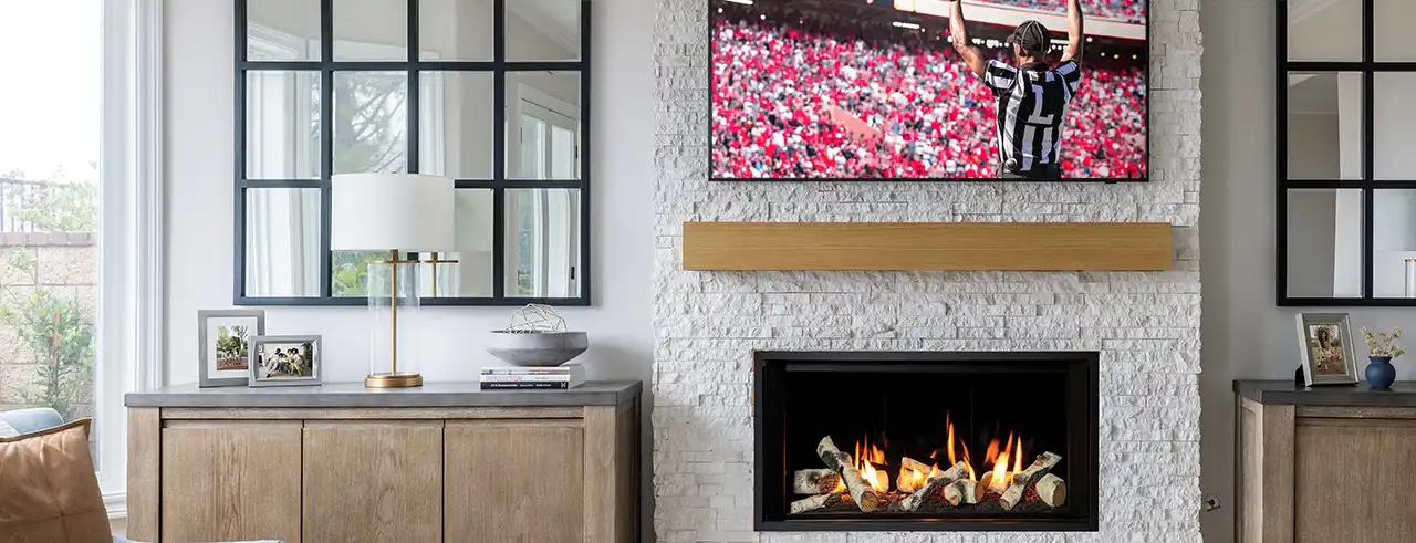 Contemporary living room with a white stone fireplace, wood mantel, and wall-mounted TV showing a football game, flanked by large black-framed mirrors and light wood cabinets.